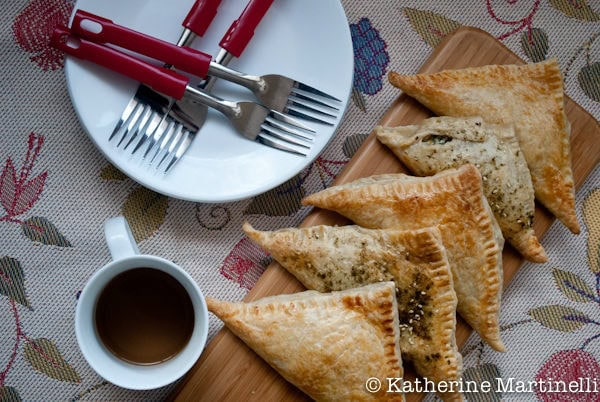 Spinach and Feta Turnovers Recipe | JustOneCookbook.com Spinach and Feta Turnovers on a cutting board with a cup of tea, and plates and forks on a table.