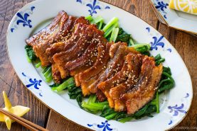 Honey pork belly slices topped with sesame seeds, served over saut&eacute;ed greens on a patterned oval platter.