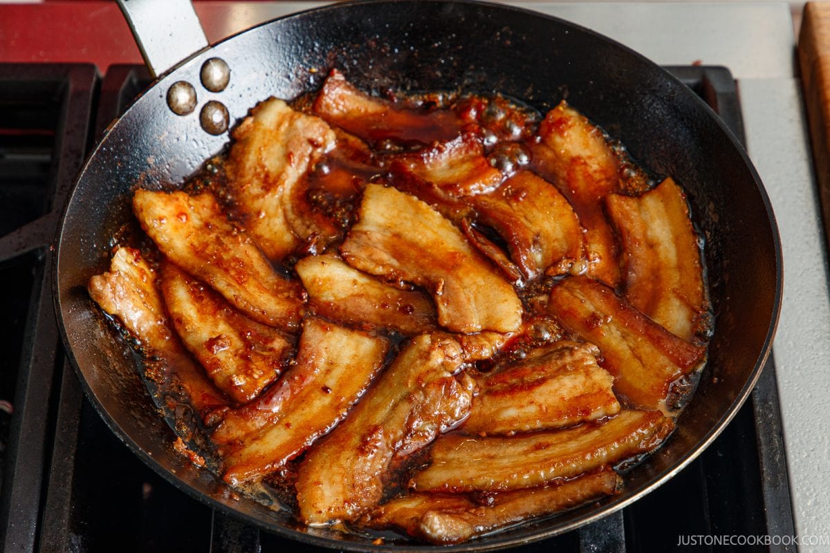 Slices of honey pork belly frying in a skillet with a dark, bubbling glaze.
