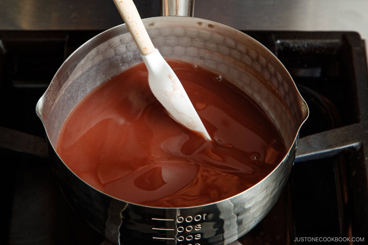 A saucepan filled with oshiruko is being stirred with a white spatula on a stovetop.