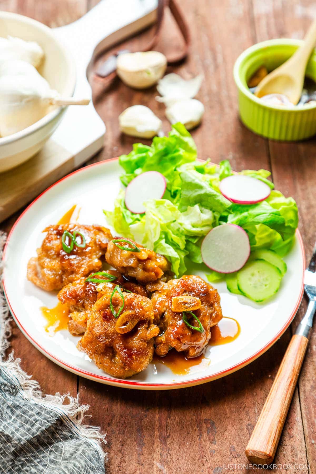 A white plate containing teriyaki pork balls and green salad.