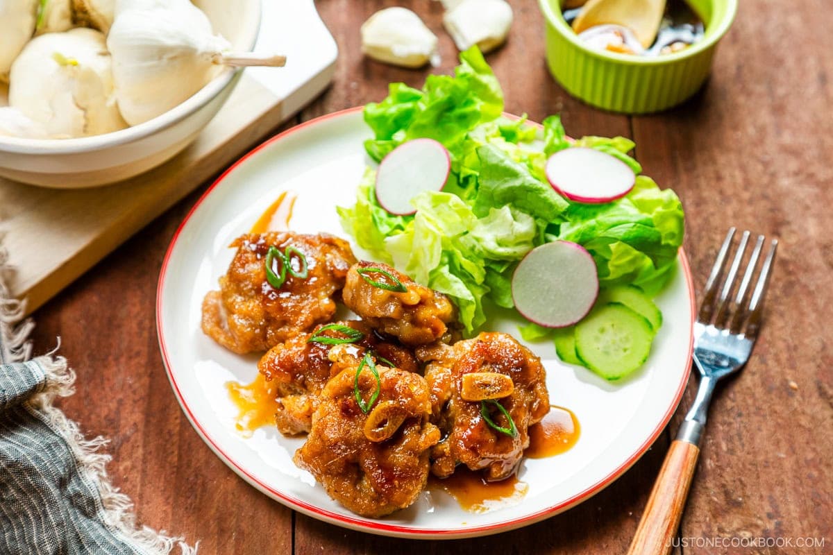 A white plate containing teriyaki pork balls and green salad.
