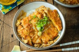 A white bowl containing Katsudon, pork cutlet rice bowl, where golden brown tonkatsu, drizzled egg, and tender onion are simmered in a savory dashi broth.