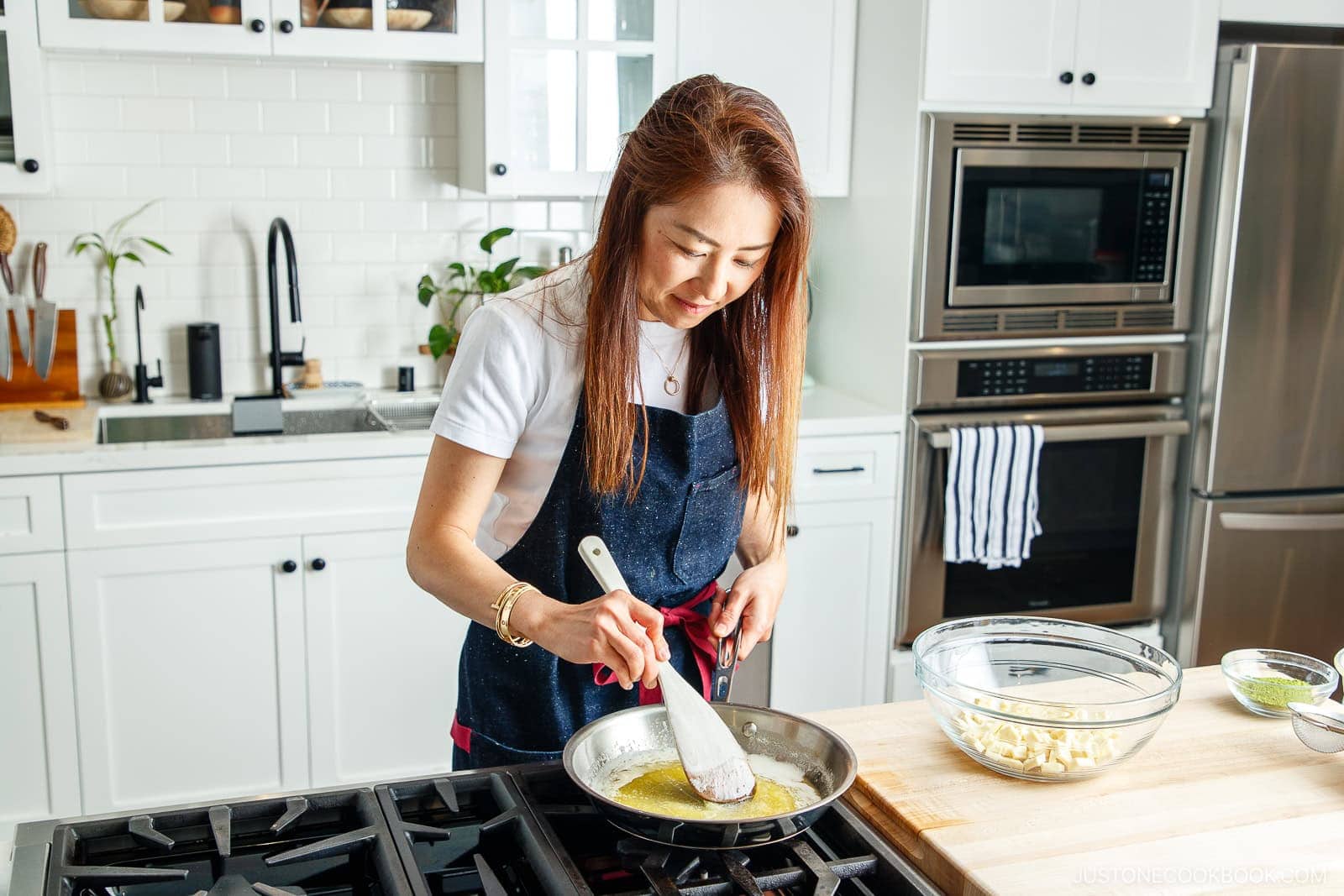 Buttered skillet with a woman cooking on a gas stove in a bright, modern kitchen, preparing a dish with melted butter and cooking utensils, showcasing Japanese cuisine and cooking tips.