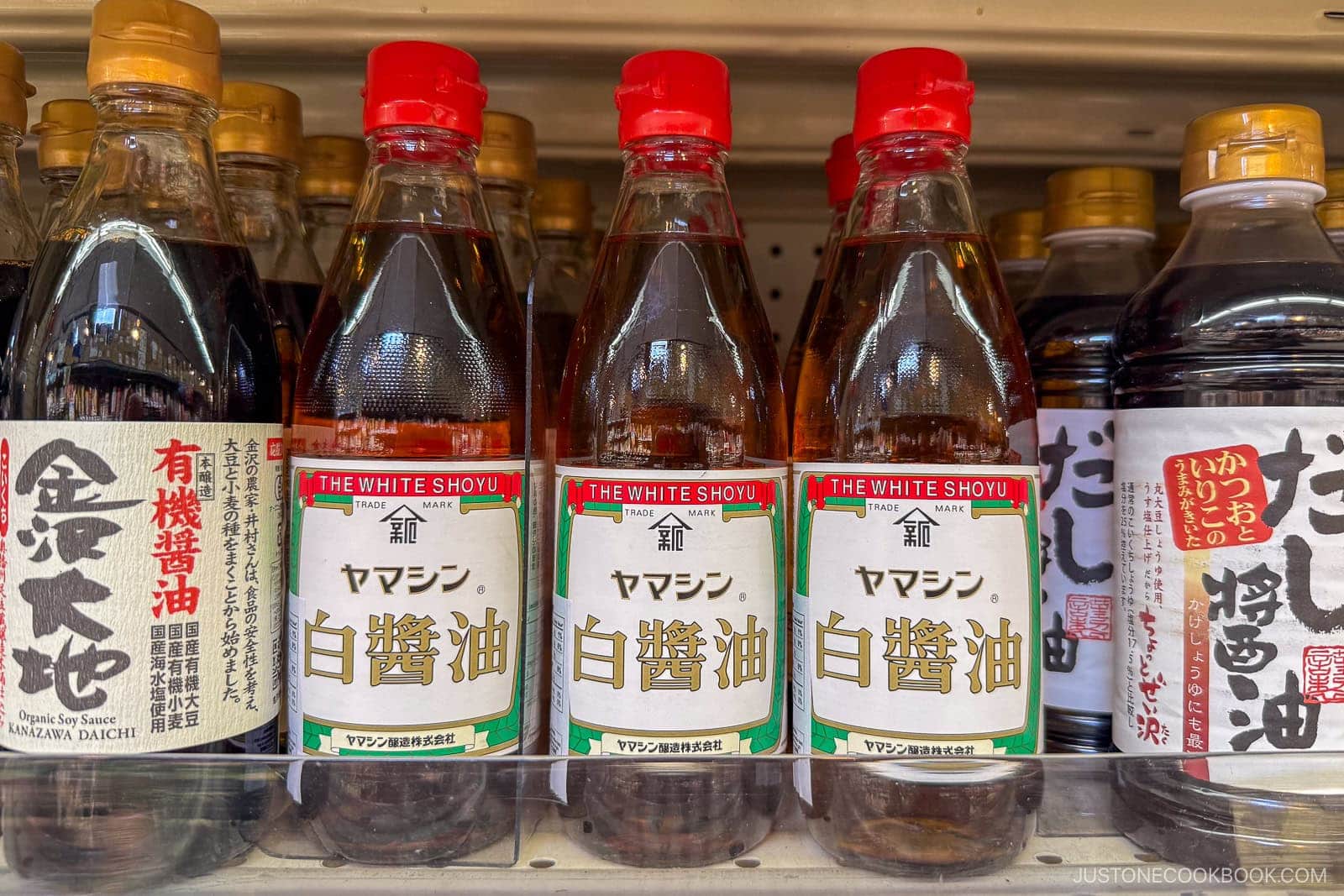 Bottles of Japanese soy sauce are displayed on a store shelf. The labels feature Japanese characters, with the central bottles reading &ldquo;The White Shoyu&rdquo; in English and Japanese.