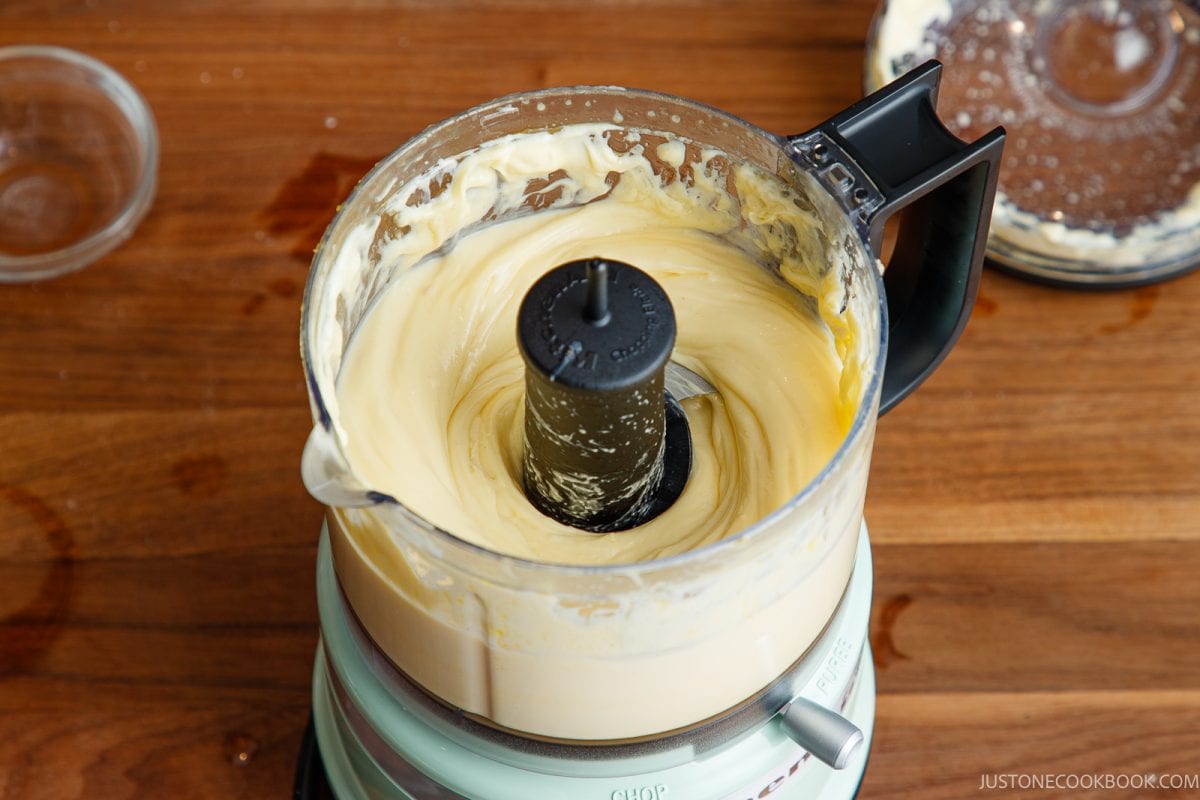 A food processor filled with smooth Japanese mayonnaise&mdash;sits on a wooden counter. The lid is off, and some batter is visible on the rim.