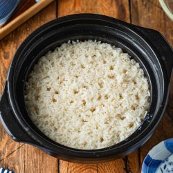 Fluffy cooked white rice in a black donabe ceramic pot on a wooden table.