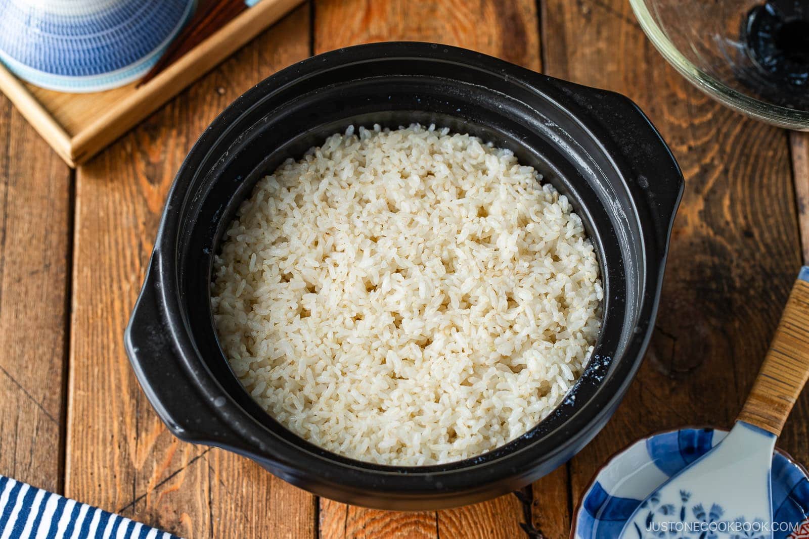 Fluffy cooked white rice in a black donabe ceramic pot on a wooden table.