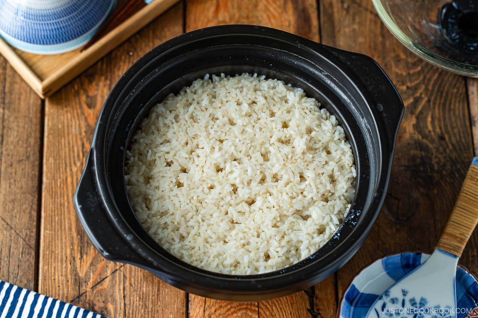 A black clay pot filled with cooked white rice sitting on a wooden table.