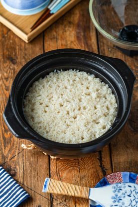 Cooked white rice in a black ceramic pot on a wooden table.