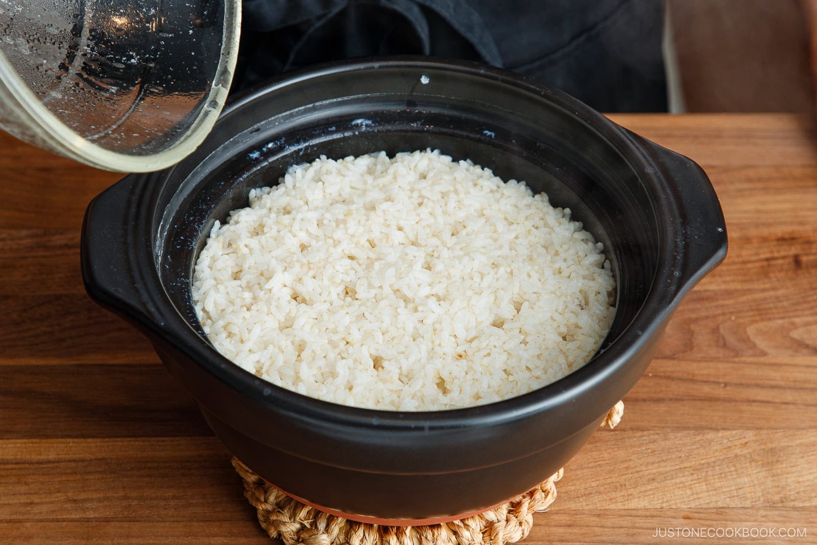 A freshly cooked pot of white rice in a black ceramic clay pot with the lid lifted.