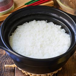 A black ceramic pot filled with cooked white rice sits on a wooden table.