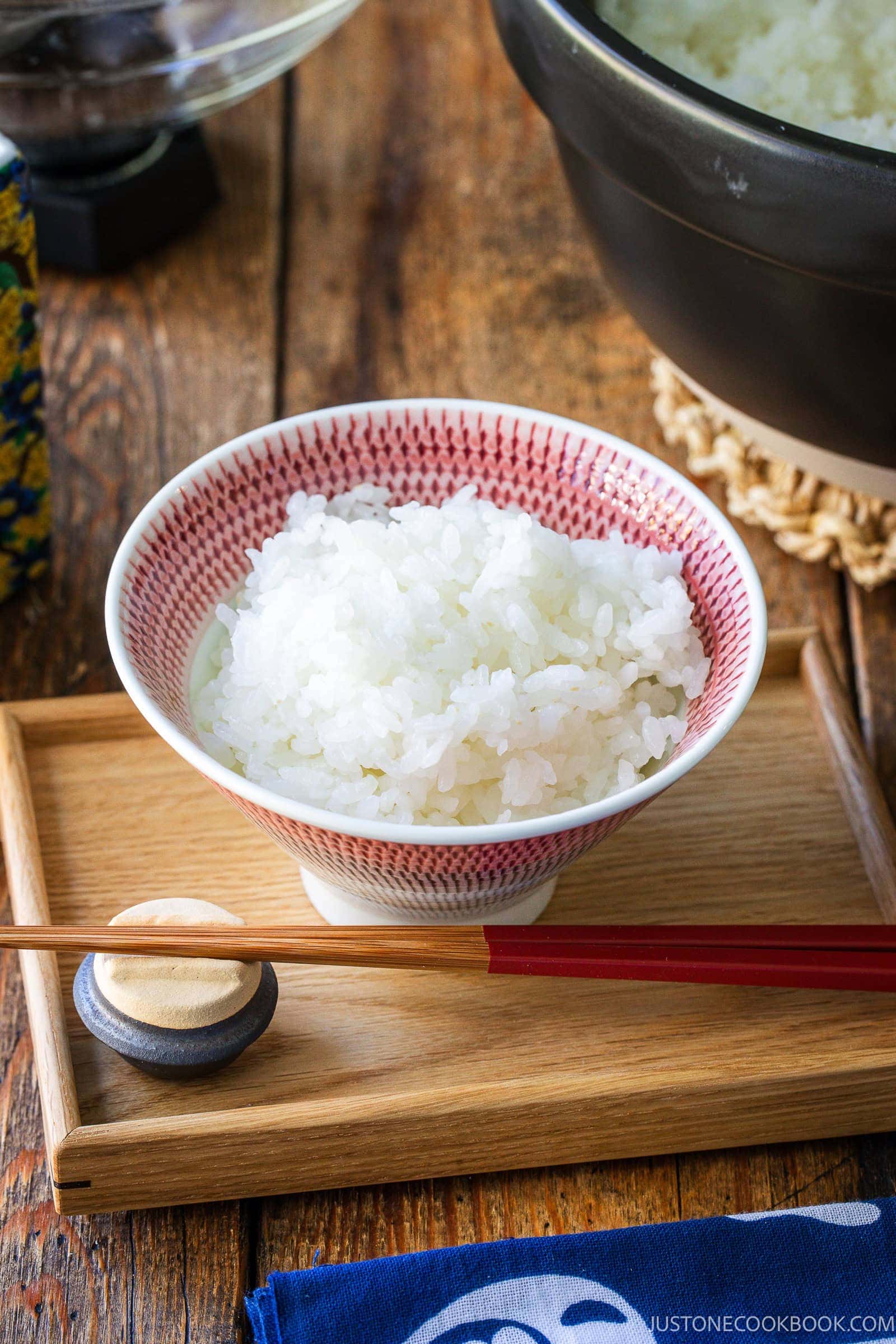 A bowl of white rice on a wooden tray with a pair of chopsticks and a chopstick rest.