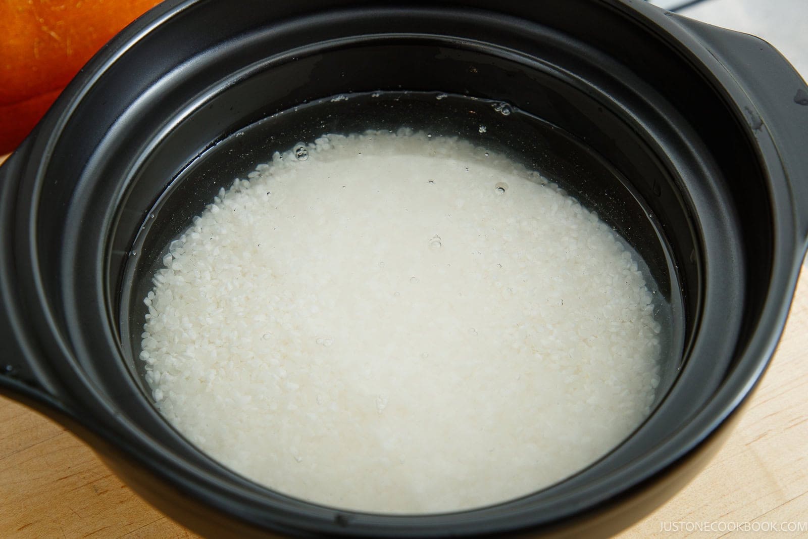 Uncooked white rice soaking in water inside a black donabe.