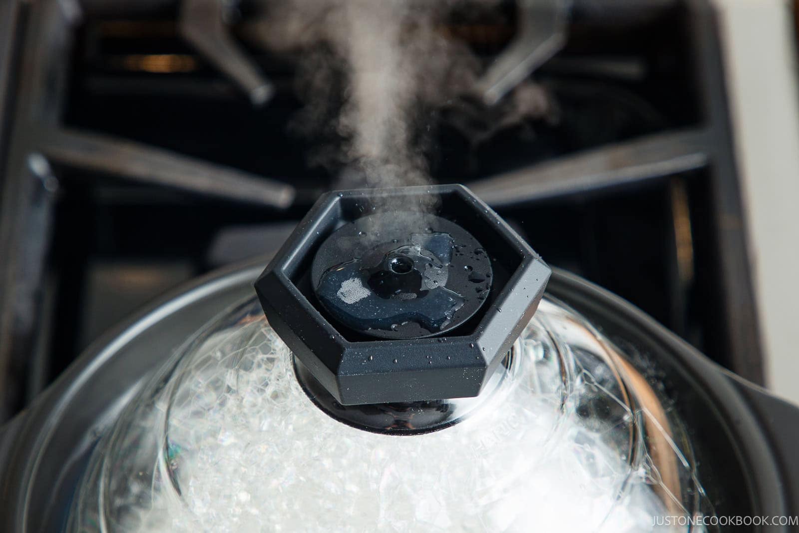 Steam escapes from the vent of a clear glass pot lid as you learn how to cook rice in a donabe on the stovetop.