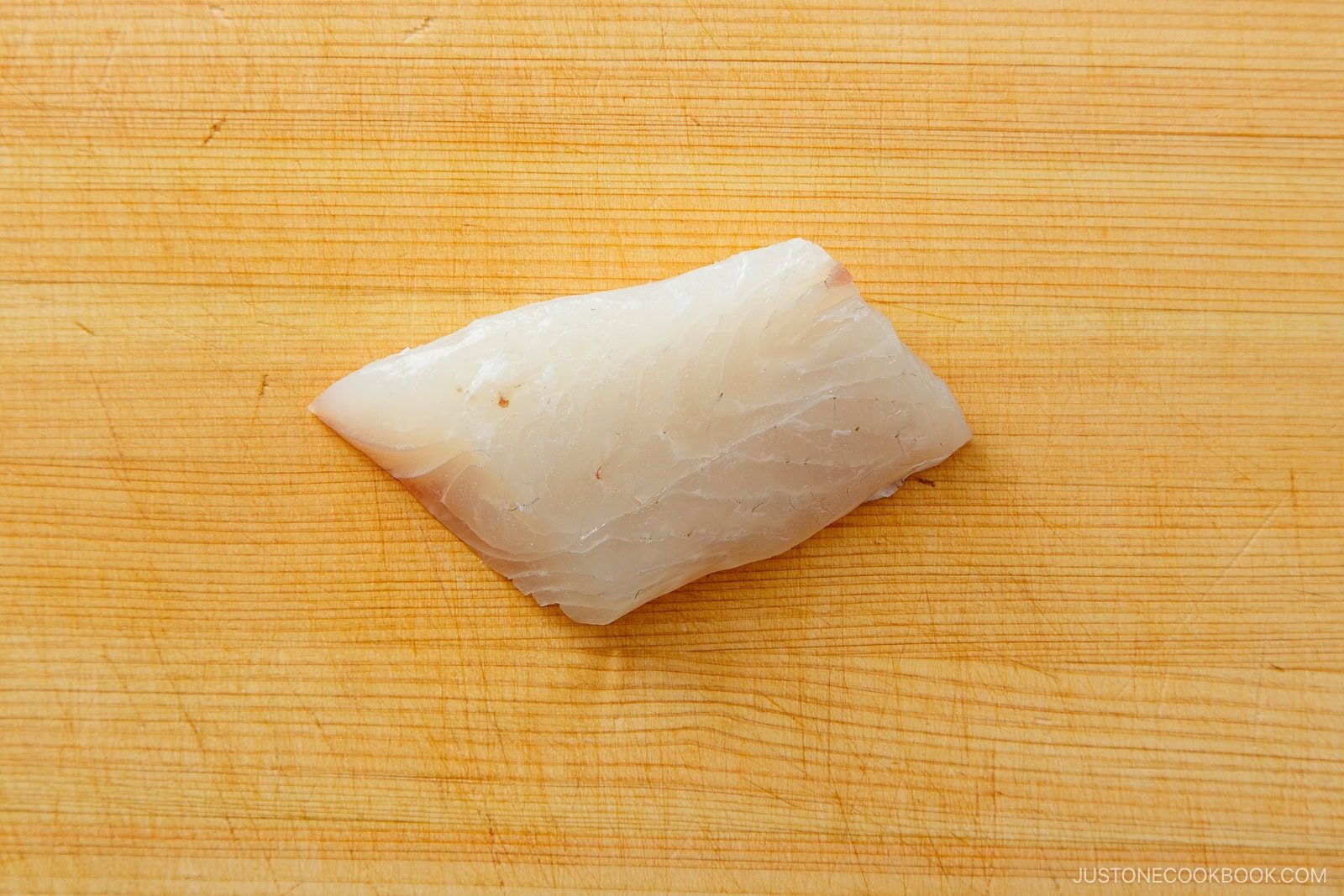 A raw fillet of white fish, ideal for learning how to cut sashimi, is placed on a light wooden cutting board.