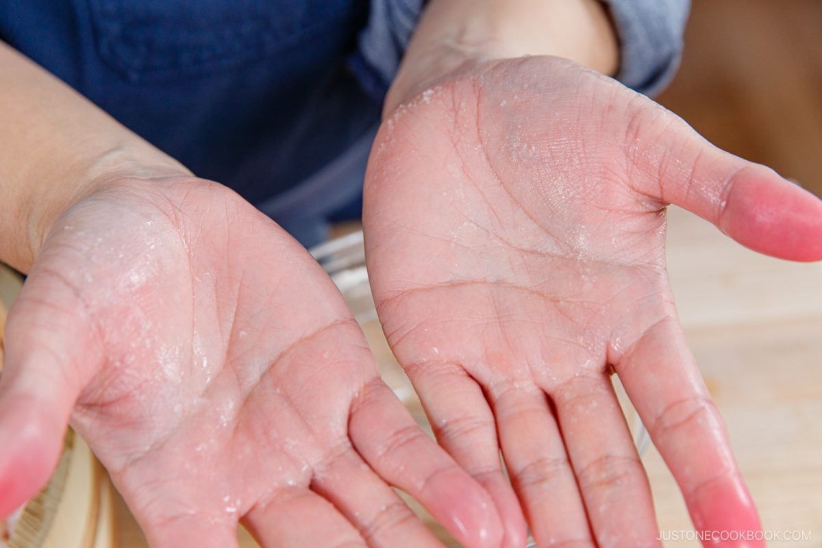 A close-up of two open hands facing up, with a light dusting of flour on the palms and fingers, likely after handling dough or shaping Umeboshi Onigiri (Plum Rice Ball) as seen in Midnight Diner.