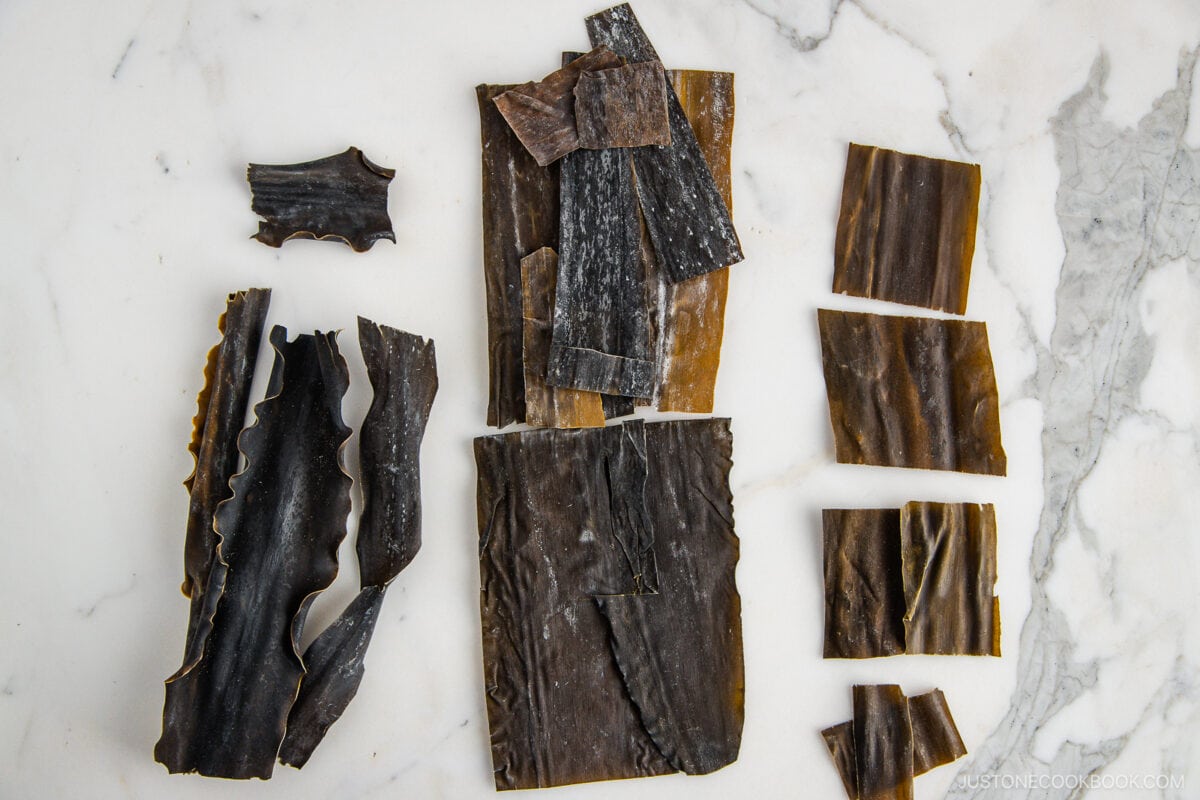 Assorted pieces of dried kombu seaweed, perfect for making Kombu Dashi, are arranged in different shapes and sizes on a white marble surface.