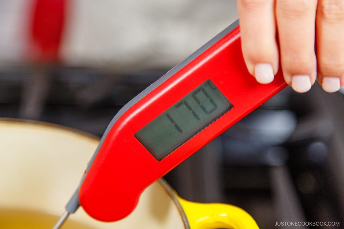 A hand holds a red digital thermometer displaying 170&deg;F over a yellow pot, checking the temperature for frying a Japanese Corn Dog.