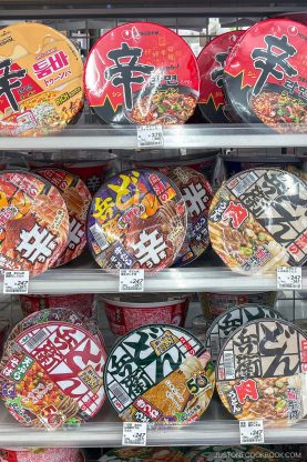 A retail shelf displaying various Nongshim and Donbei instant noodle bowls with Japanese price tags, perfect for those seeking new instant ramen hacks.