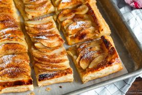 Easy Apple Tart: Rectangular slices of apple tart with flaky crust, topped with thinly sliced apples, cinnamon, and powdered sugar, arranged on a baking sheet lined with parchment paper.