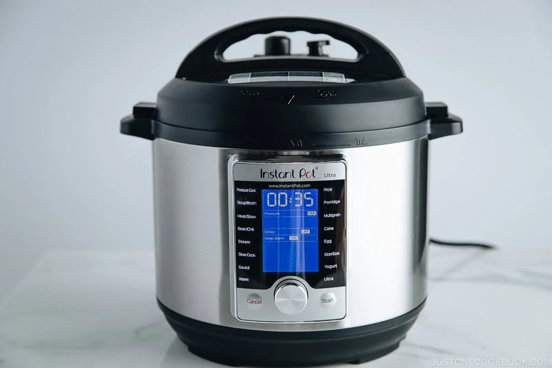 A stainless steel Instant Pot Ultra electric pressure cooker sits on a white surface with its digital display showing 00:35. The lid is closed and the control panel is illuminated, ready to prepare a comforting batch of Japanese chicken curry.