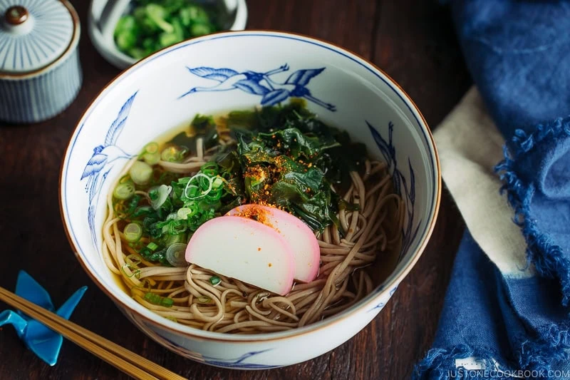 A Japanese bowl containing Toshikoshi Soba Noodle Soup with fish cake and wakame seaweed.