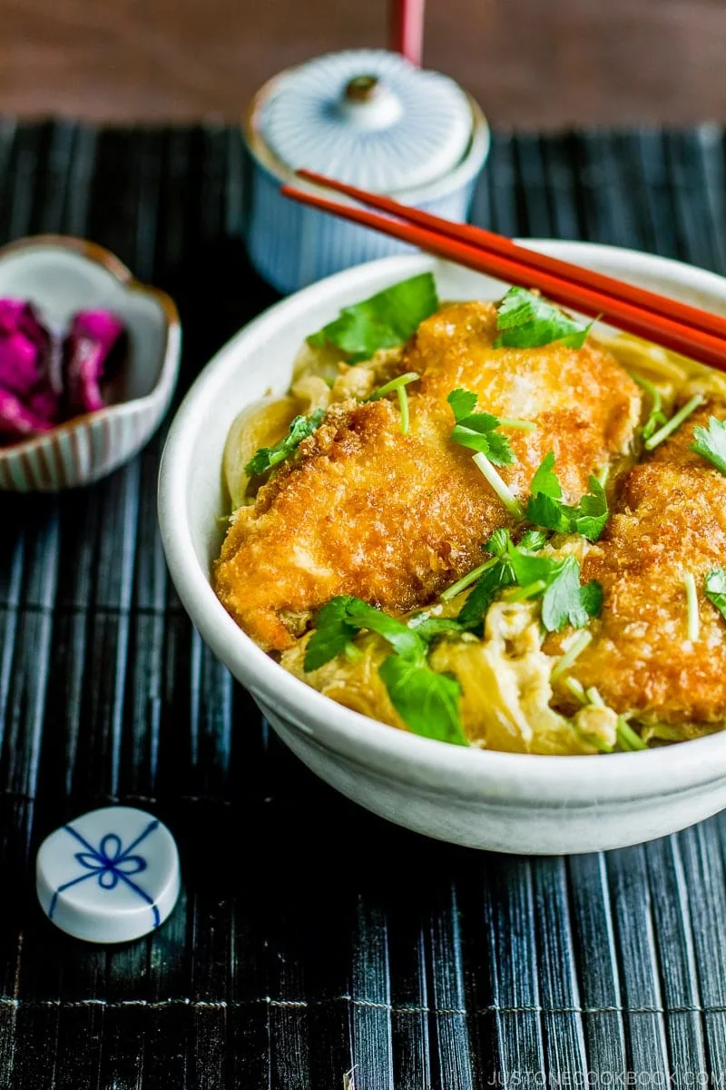A white large donburi bowl containing steamed rice topped with chicken katsu, egg, and onion cooked in the savory seasoning.