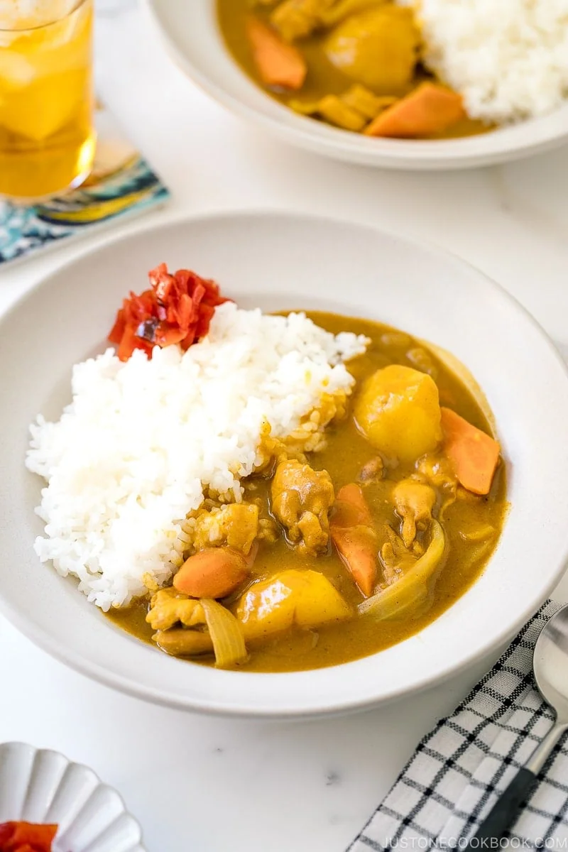 A bowl of Japanese chicken curry with chunks of chicken, carrots, and potatoes served alongside white rice, garnished with pickled ginger.