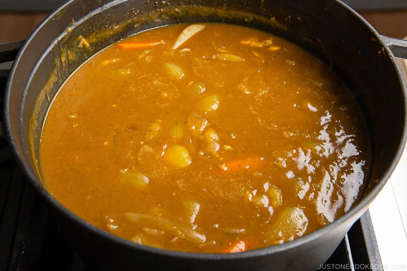 A pot of Japanese chicken curry with visible chunks of potatoes, carrots, onions, and tender pieces of chicken in a thick, golden-brown sauce, simmering on a stovetop.
