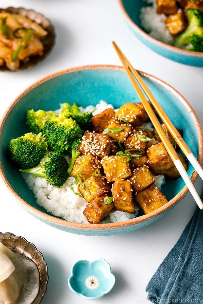 A taquoise bowl containing teriyaki tofu and broccoli over steamed rice.