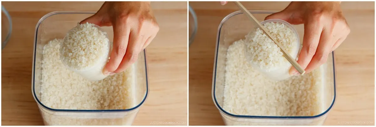 A hand scoops rice into a measuring cup, then levels it with a chopstick over a clear container full of rice on a wooden surface, preparing the perfect amount for making onigiri.