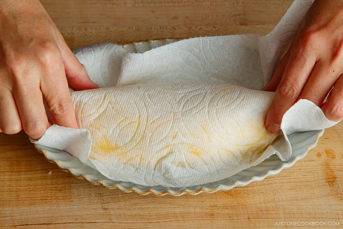 Omelette rice on an oval serving plate with paper towel over it. Hands shape it into a rugby ball shape for Omurice (Japanese Omelette Rice).