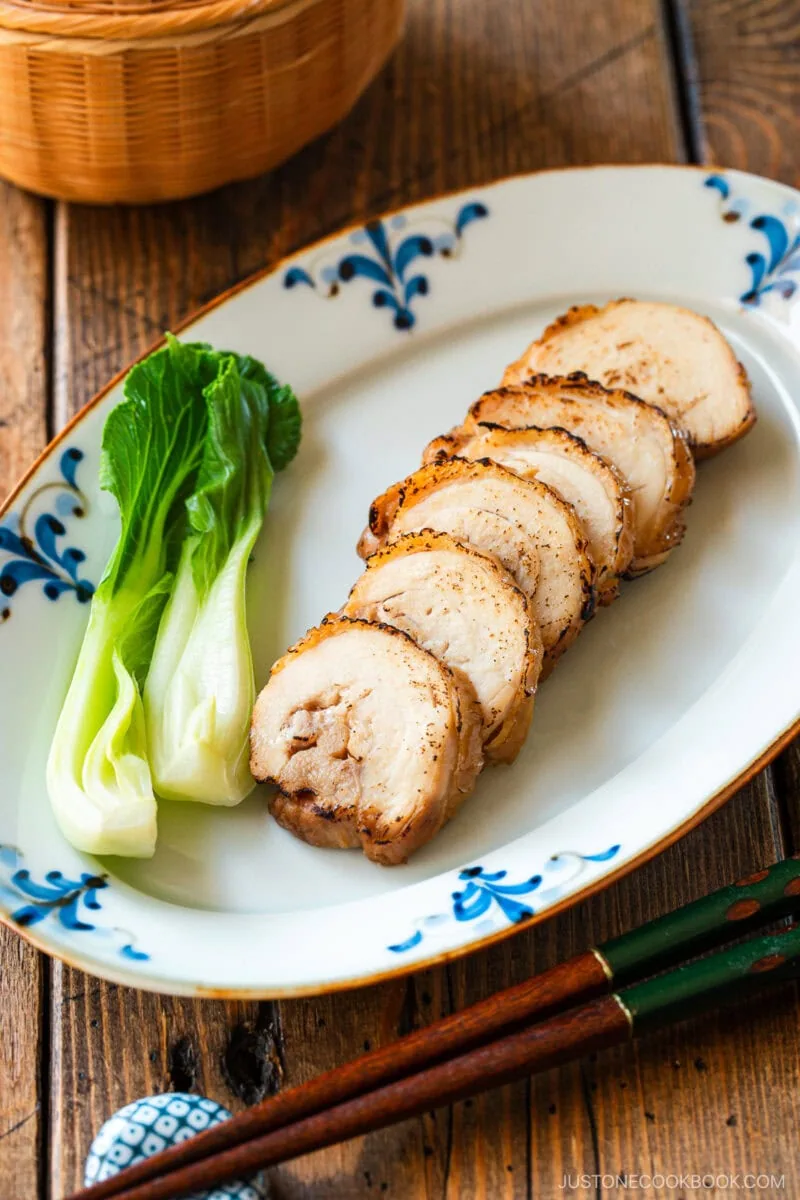A rectangular plate containing thinly sliced, seared chicken chashu served with bok choy.