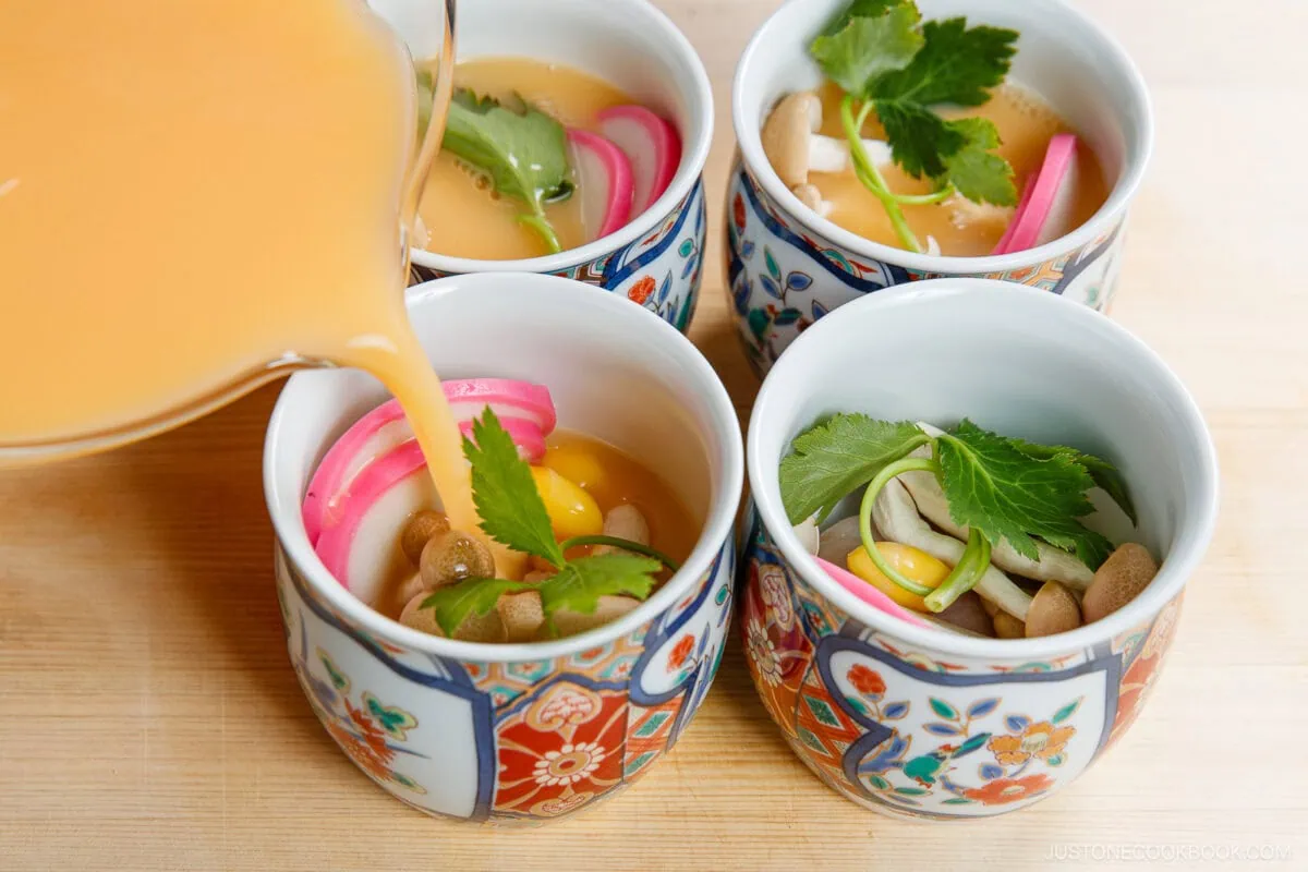 Delicious Japanese savory steamed egg custard served in traditional cups, garnished with fresh herbs and colorful toppings, perfect for a refined appetizer or snack.