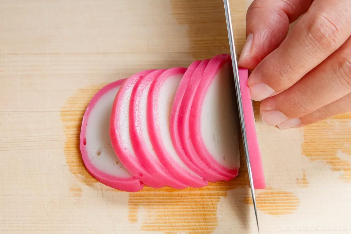 Thinly sliced pink and white kamaboko fish cake on a wooden cutting board.
