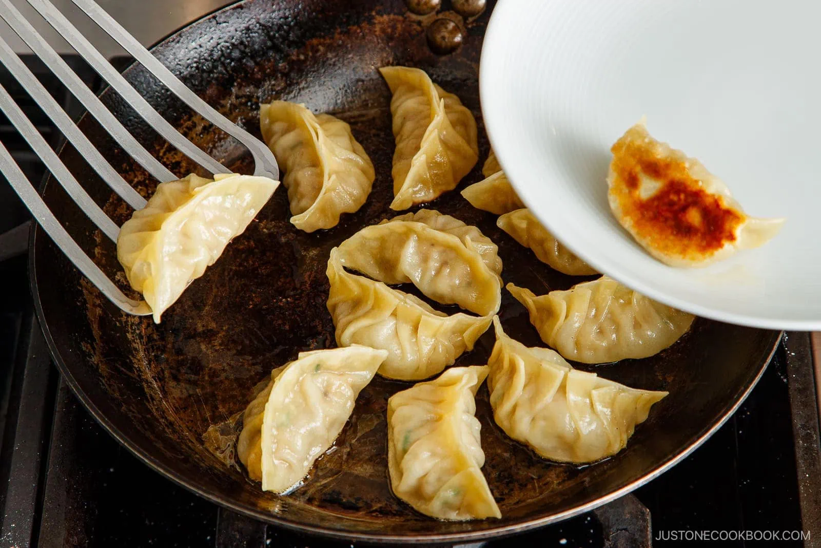 A spatula lifts golden-brown pan-fried dumplings from a skillet, while a plate holds one crispy gyoza, showcasing the delicious results of this easy Gyoza Recipe, ready to be served.